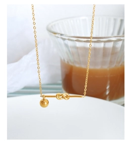Detail of minimalist gold knotted necklace with a metallic bead over coffee scene
