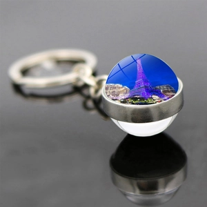 Macro detail of Eiffel Tower glass ball keychain with purple lights on dark blue night view