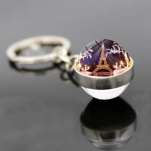 Macro shot of Eiffel Tower glass ball keychain with golden lights on a black mirror base