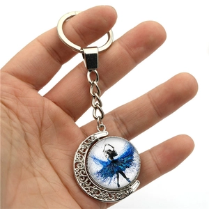 Detail of a silver moon-shaped keychain featuring a ballerina silhouette in a blue dress