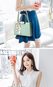 Détail d'un sac à main en cuir vert clair avec foulard en soie et logo en métal doré