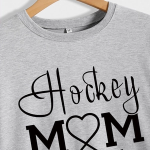 Grey Hockey Mom sweatshirt with heart design on a wooden hanger, close-up texture