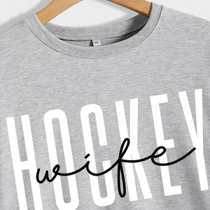 Grey crewneck sweatshirt featuring a white HOCKEY wife print on a wooden hanger