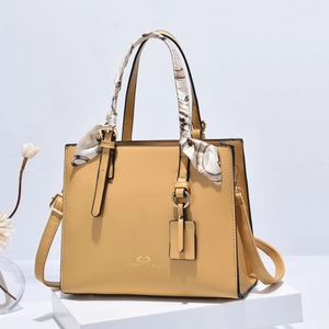 Detail of yellow handbag with silk scarf, gold logo, and adjustable shoulder strap