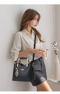 Detail of black leather handbag featuring golden leaf pendant and metallic chain handle