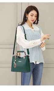 Deep green leather handbag with gold leaf charm shown on a fashion model