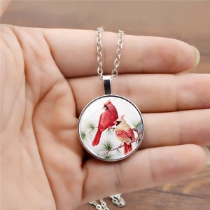 Close-up of silver-tone necklace featuring two red cardinal birds on a round pendant