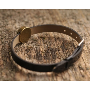 Retro black leather adjustable bracelet with bronze metal charm on a rustic wood surface