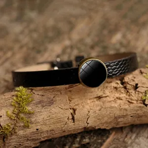 Handmade black leather bracelet with bronze round tray base on natural wood background