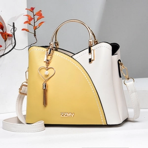 Detail of yellow and cream contrast bucket bag with gold metal handle and heart pearl tassel