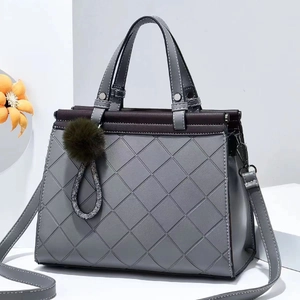 Quilted grey tote bag with top handle and green pompom charm on a white minimalist background
