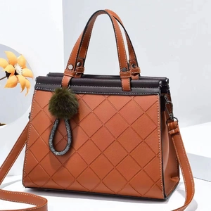 Detail of quilted leather tote bag with brown handles and a green pompom charm