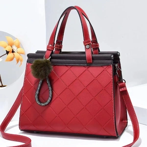 Red quilted tote bag with black handles, adjustable shoulder strap and green pompom charm