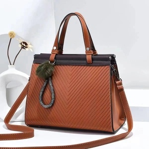 Detail of brown quilted tote bag with V-shaped stitching and green fur pompom charm
