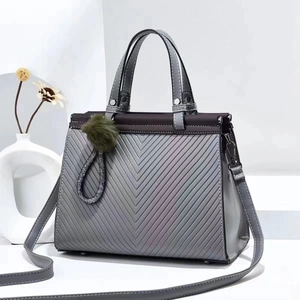 Detail of grey quilted tote bag with V-shaped embossing and green fur ball charm