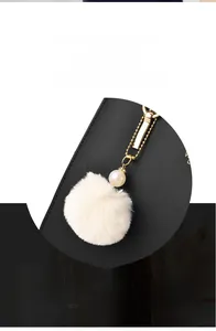 Detail of white fluffy pompom charm with pearls and gold chain on black leather handbag