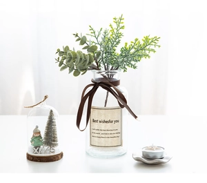 Close-up of artificial pine greenery, glass vase, and Christmas decor on a white table