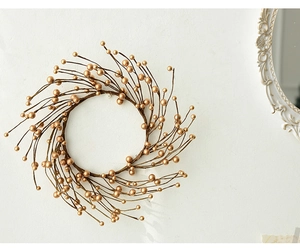 Detail of a sparkling gold berry wreath hanging on a white wall for Christmas decor