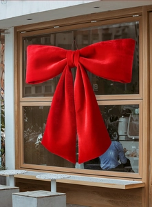Close-up of large red velvet bow ornament hanging on a wooden window for festive decoration