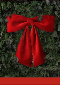 Detail of a large red velvet Christmas bow hanging on green pine branches for decoration