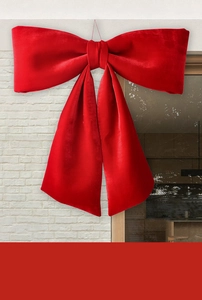 Close-up of extra large red velvet bow hanging on a white wall for festive decoration
