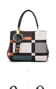 Detail of color-block plaid handbag showing KUOY gold logo and fuzzy pompom charm