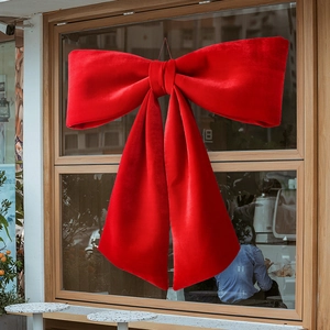 Large red velvet Christmas bow decoration hanging on a wooden glass window pane