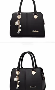 Detail view of black lychee grain handbag with golden hardware and floral pendant