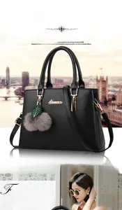 Detail of black faux leather handbag with dual handles and plush ball leaf charm