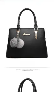 Close-up of black leather handbag with gold logo and grey faux fur pompom charm