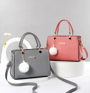 Detalle del bolso de piel sintética con amuleto de corazón y llavero de pompón decorativo