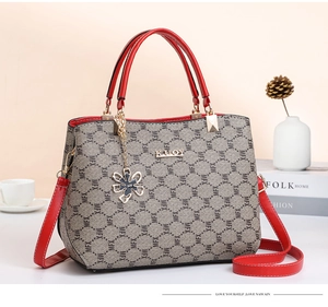 Chic grey monogram tote with red leather straps and floral charm in an elegant setting