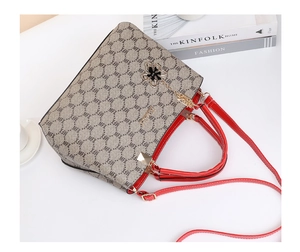 Close-up of a grey patterned handbag with red handles and flower charm on a white table