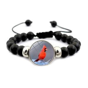 Detail of black matte beads and cardinal bird glass cabochon on adjustable woven bracelet
