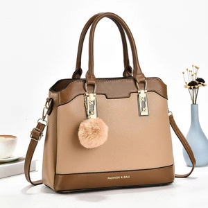 Chic two-tone brown and beige PU leather shoulder bag with plush charm on a desk