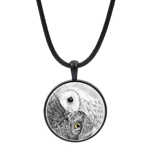 Macro detail of round glass owl pendant necklace with black woven rope and metal frame