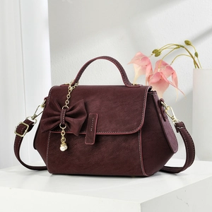 Luxurious wine red crossbody bag with bow decoration and pearl pendant on a white platform