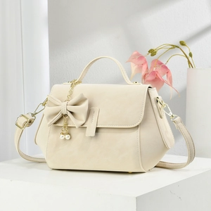 Elegant cream white crossbody bag with decorative bow and pearl pendant on a minimal display