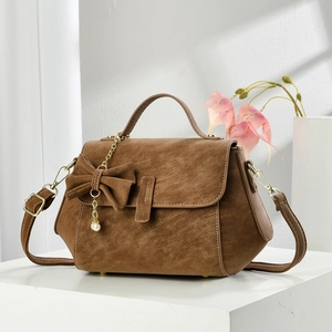 Elegant brown vintage satchel bag with pearl charm and bow on white podium stand