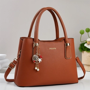 Détail du cuir grainé marron caramel avec logo doré et pendentifs métalliques de luxe