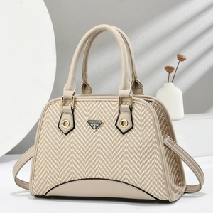 Detail of beige shell handbag showing textured herringbone weave and metal logo plate