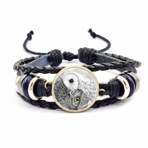Détail d'un bracelet en cuir tressé multicouche avec breloque hibou en verre rétro