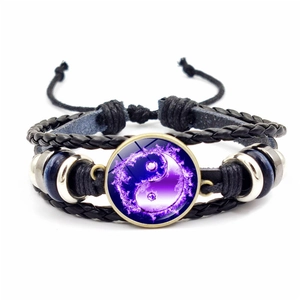 Détail d'un bracelet en cuir noir tressé avec breloque Yin Yang violette et perles