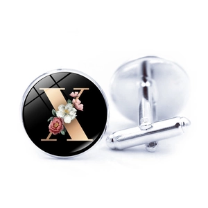 Close-up of silver-tone cufflinks featuring a black base with gold letter X and floral patterns