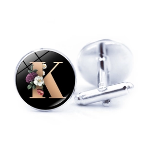 Silver letter K cufflinks with gold font and floral design on black background