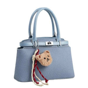 Sac à main bleu tissé avec serrure métallique et charm ours mignon sur fond blanc neutre