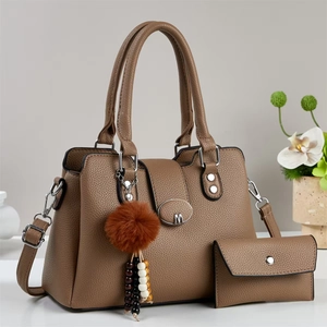 Détail du sac à main marron en cuir grainé avec boucle en métal M et pendentif pompon