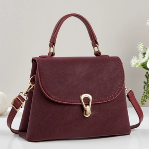 Détail d'un sac à main bordeaux en cuir texturé avec fermoir doré et poignée haute
