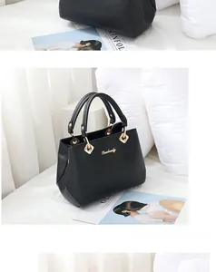 Detail of black matte leather tote bag with gold hardware on white bedding