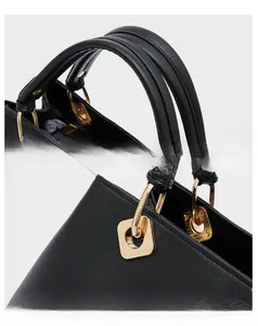 Close-up of black leather handbag featuring reinforced top handles and golden metal buckles